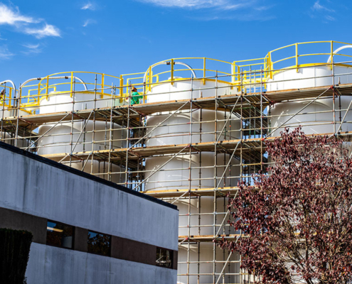 Side view of tanks with scaffolding around them, in process of being painted